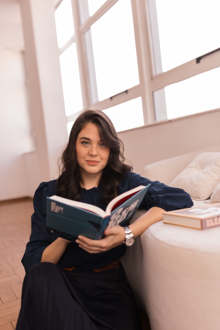 Faíla Thomé lendo, sentada em um sofá claro