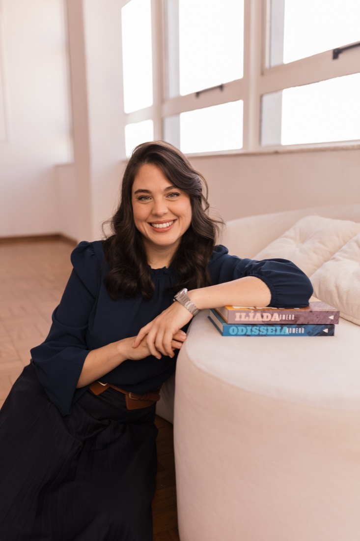 Faíla Thomé sorrindo, apoiada em uma pilha de livros