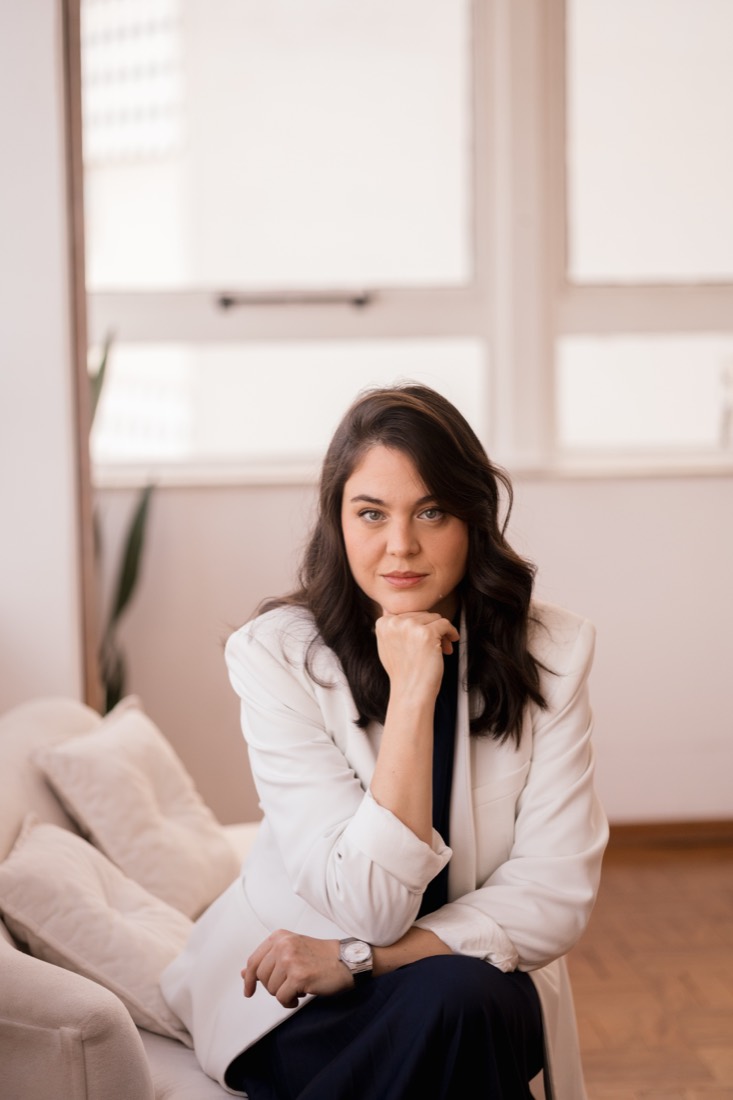 Faíla Thomé de blazer claro, sentada em uma poltrona